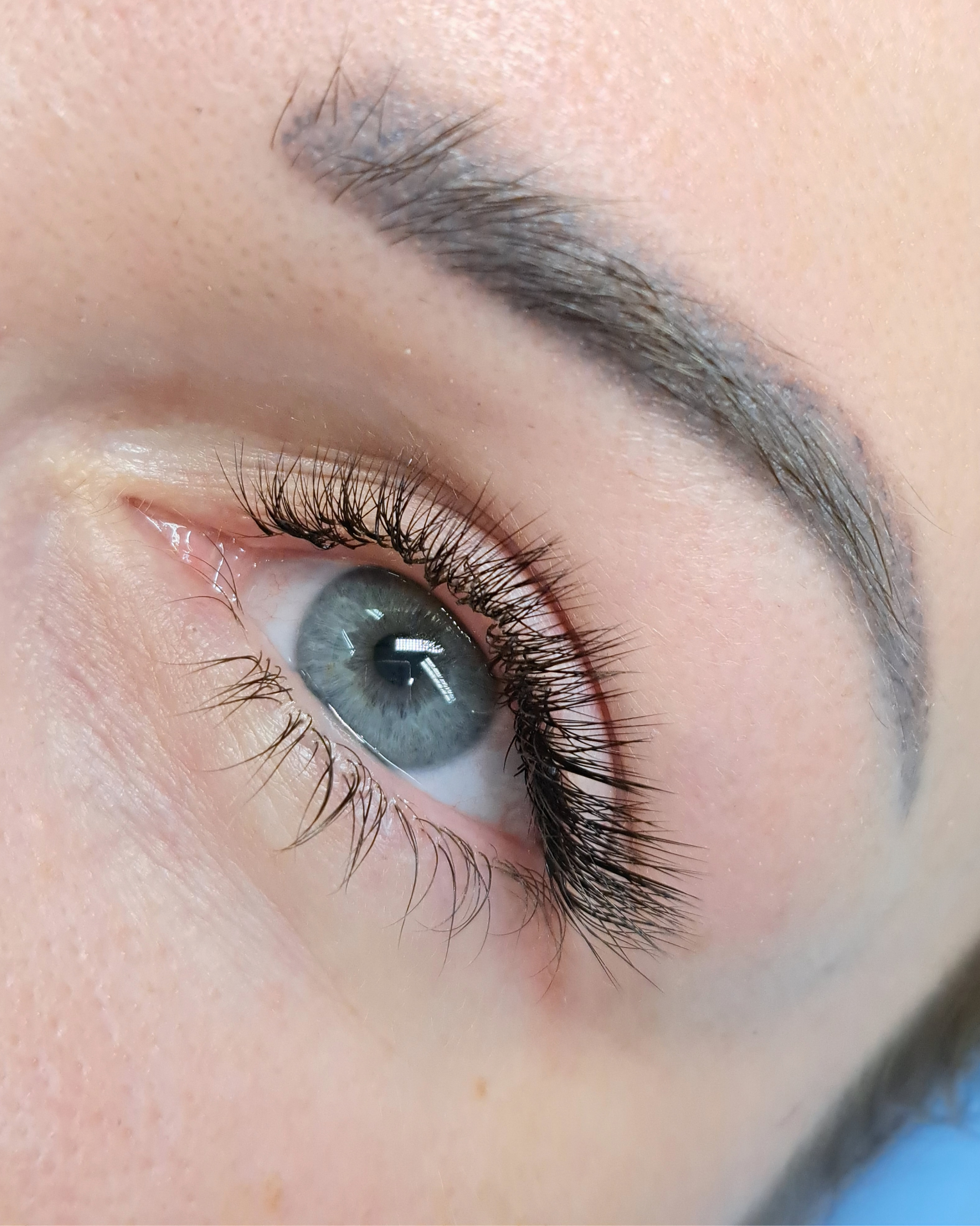 Close-up of a human eye with blue iris, long eyelashes, and a well-defined eyebrow.