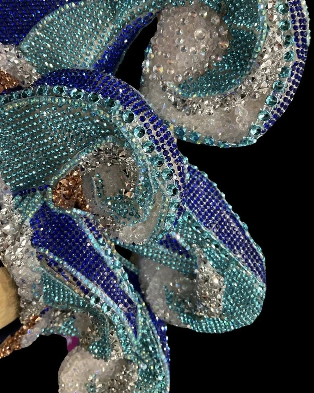 Close-up of a decorative object adorned with multicolored rhinestones arranged in intricate swirling patterns.