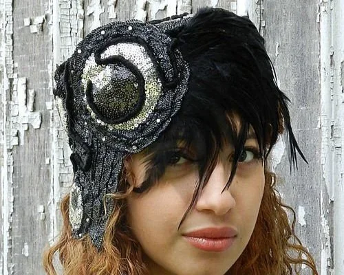 Woman wearing a black and silver sequin hat with a large flower design, standing in front of a weathered white wooden background.