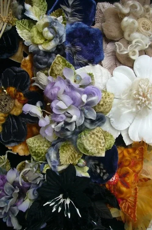 A collection of decorative fabric flowers in various colors including purple, white, black, gold, and beige.