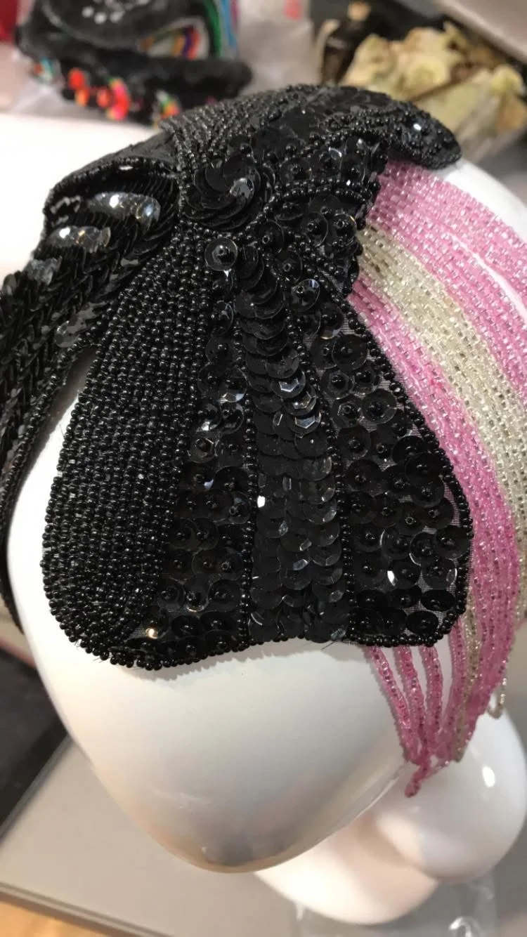 Close-up of a decorative headband with black sequins and beads on one side, and pink and white beads on the other, resting on a white mannequin head.