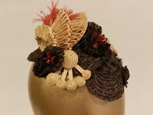 A decorative hair accessory featuring fabric flowers in beige and dark colors with red accents, attached to a gold-colored hair comb.