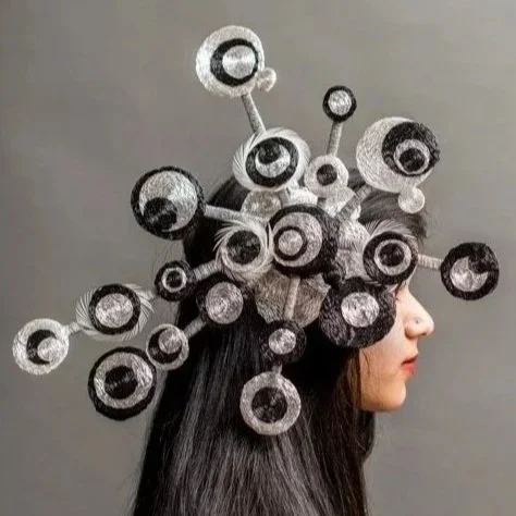 Woman wearing a headpiece designed to look like a molecular structure with black and white circular elements connected by rods.
