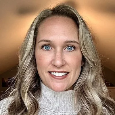 A woman with long blonde hair and blue eyes smiling in a close-up portrait.