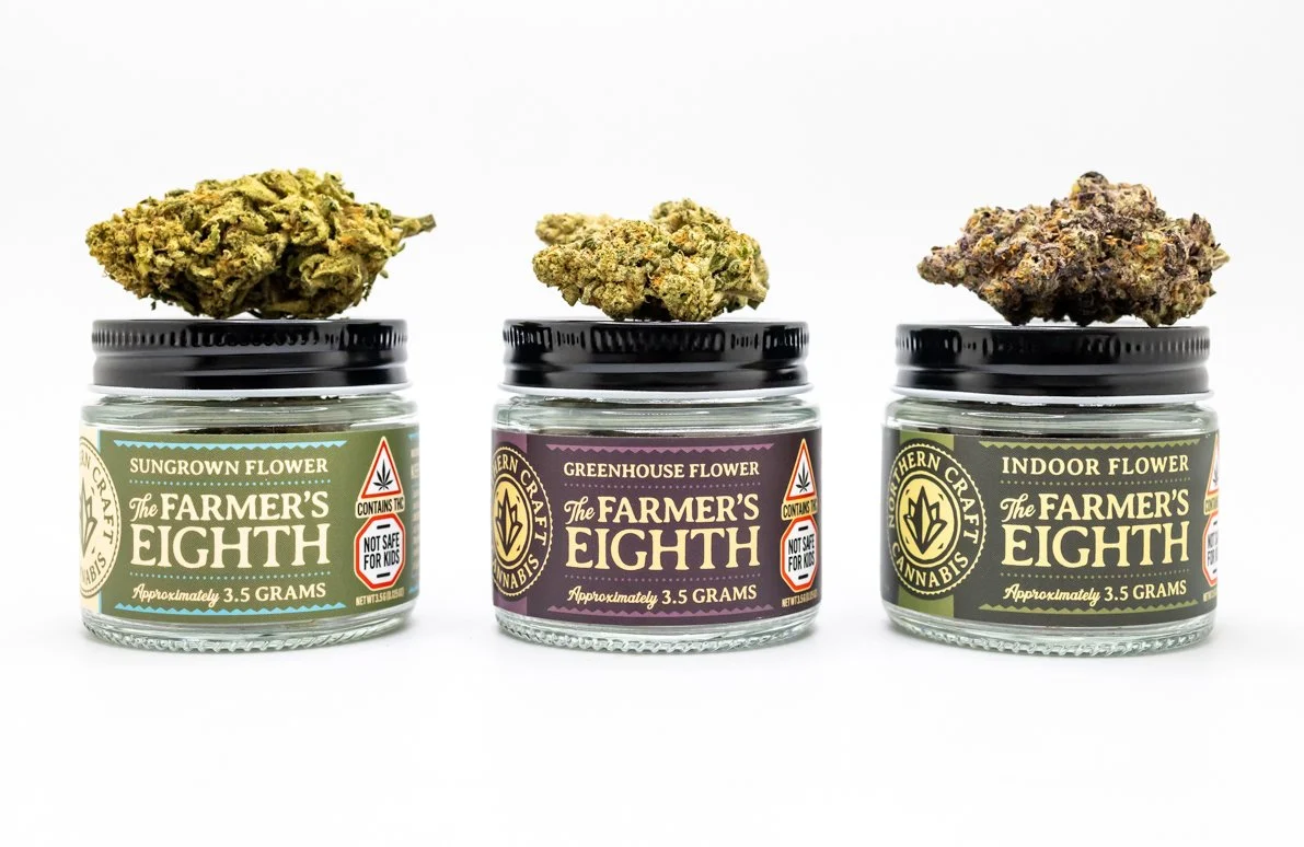 three jars of cannabis with one nug of green cannabis sitting on top of each lid
