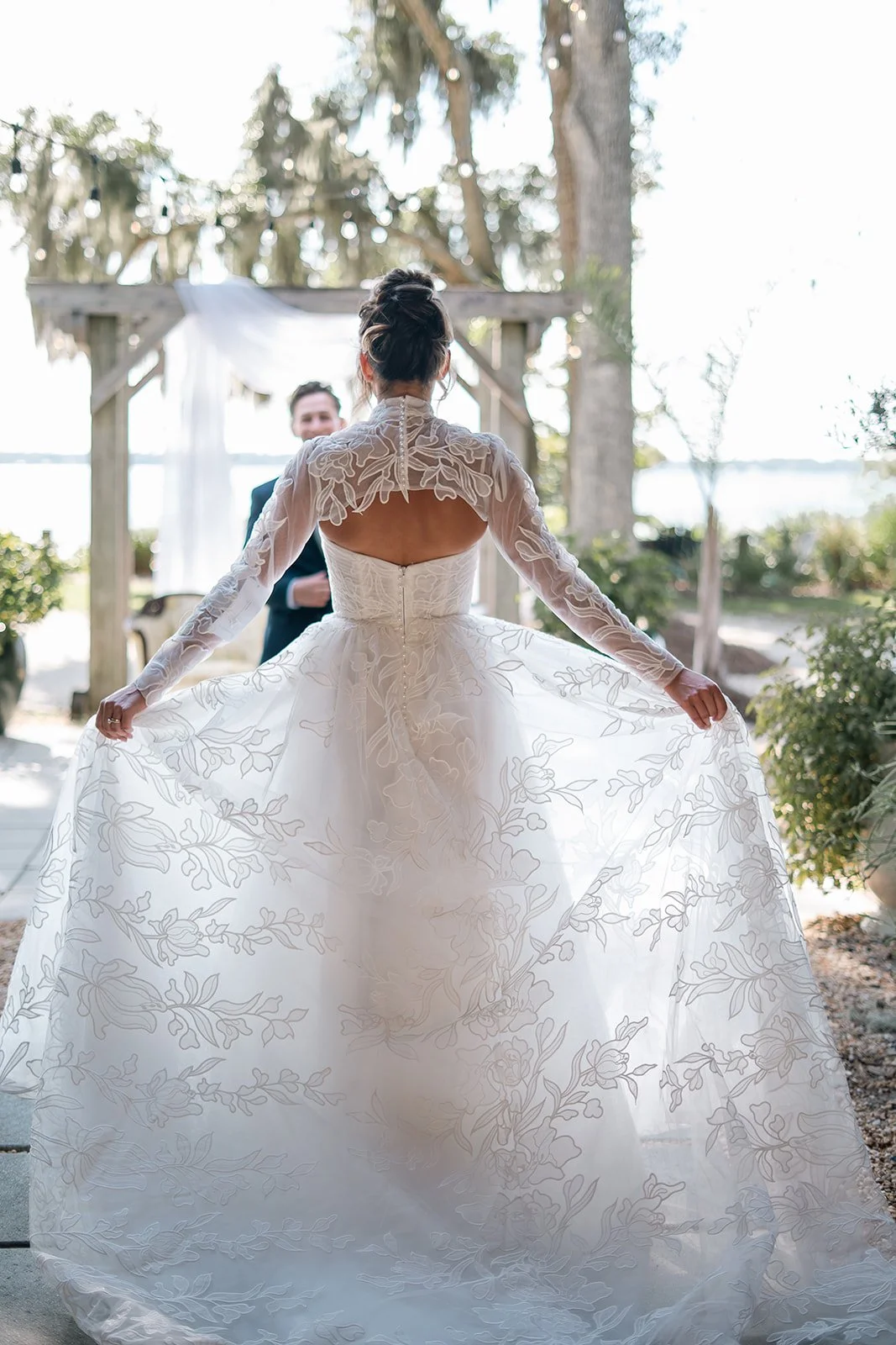 Cinematic back view of a bride lifting her skirt in a vintage dress with the groom blurred in the distance — editorial elopement style. by karen fabiola photo