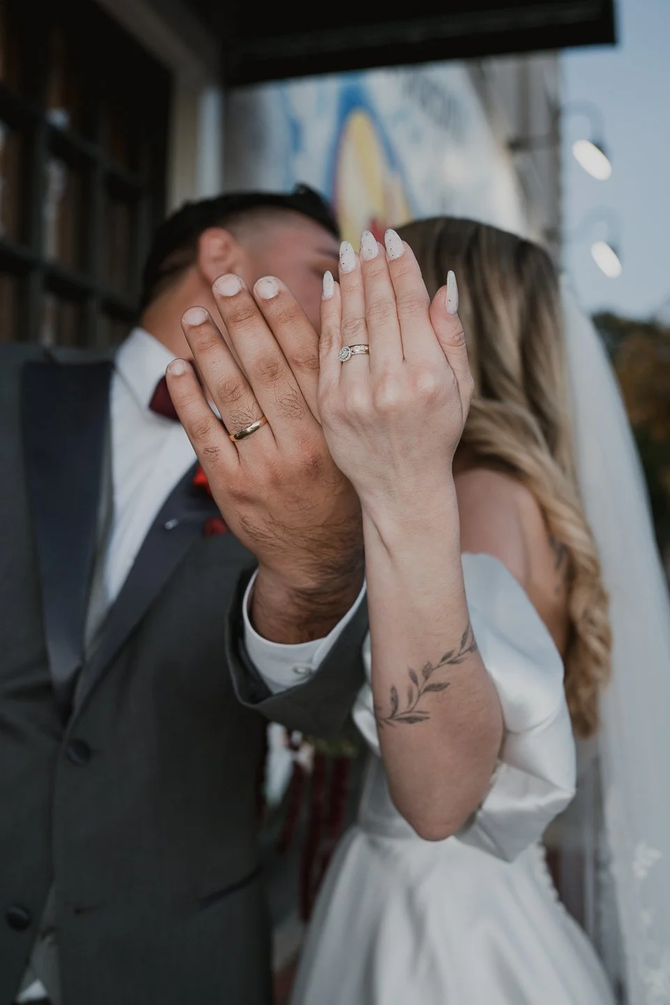 Playful and artistic moment of a bride and groom holding up their hands to showcase their wedding rings while gently covering their faces, captured by Karen Fabiola Photo. This candid image highlights intimacy, personality, and modern romance, perfec