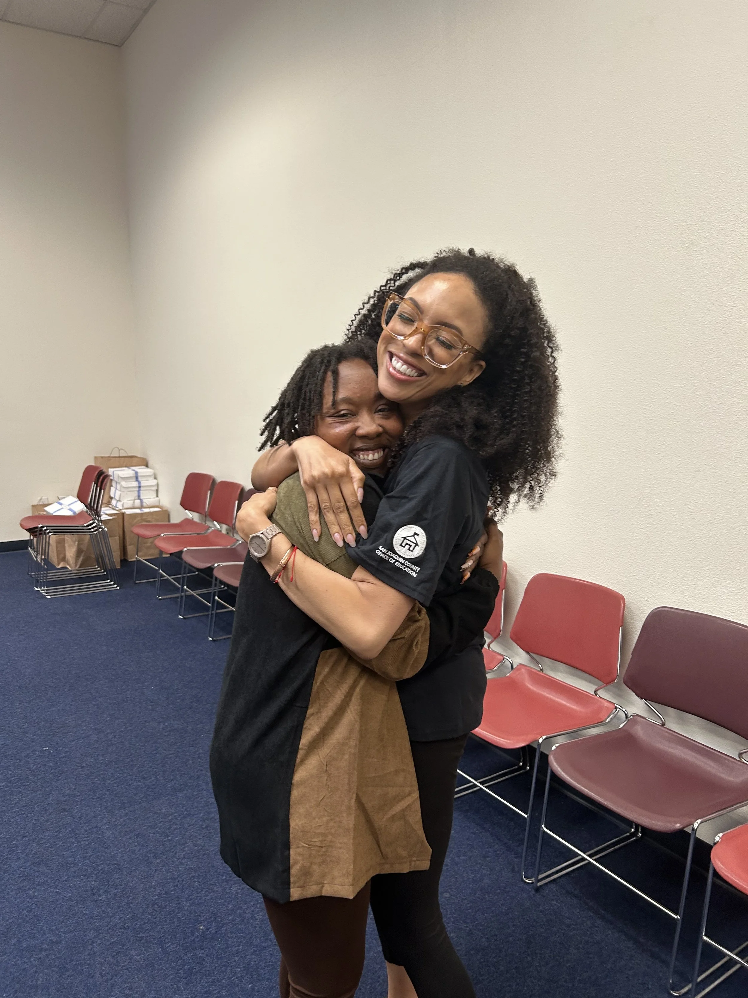 MelRo hugging a student and smiling in a room with rows of chairs.