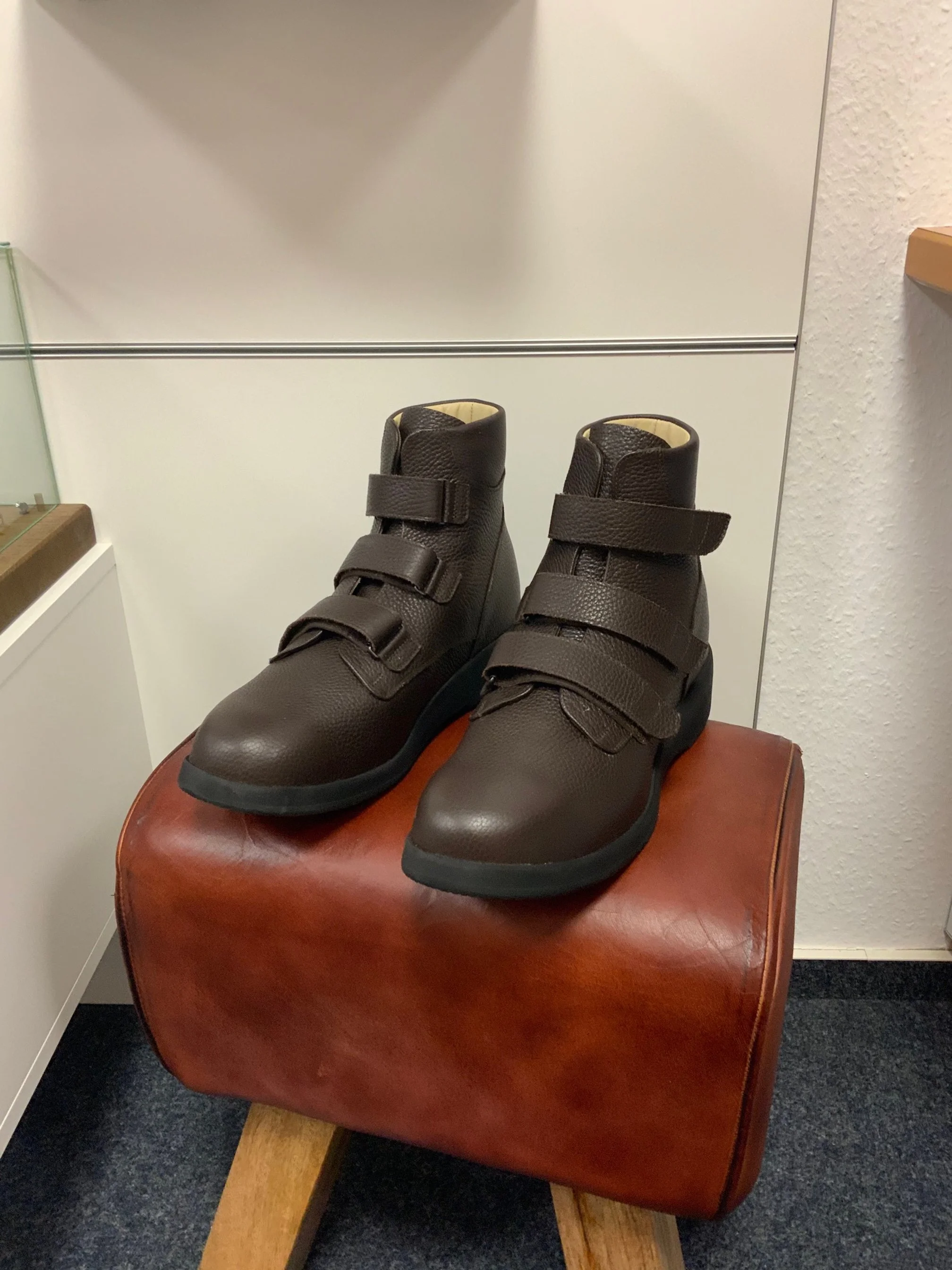 Blaue Wanderschuhe mit Klettverschlüssen auf einem braunen Hocker in einem Raum.