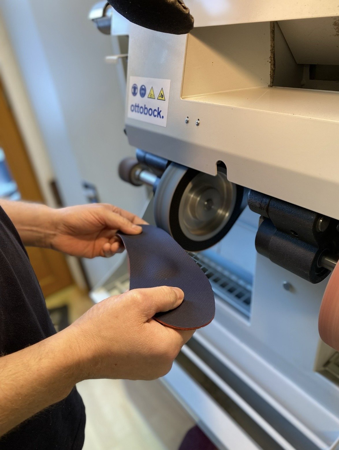 Eine Person hält eine orthopädische Einlage an eine Schleifmaschine, die vermutlich zum Schneiden oder Polieren genutzt wird, mit einem Aufkleber der Marke ottobock.