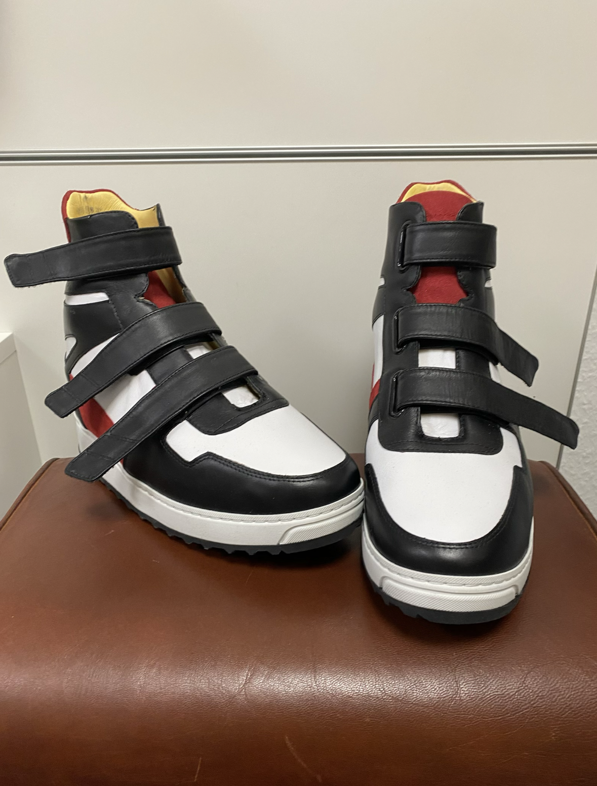 Ein Paar Sportschuhe in Schwarz, Weiß, Rot und Gelb mit Klettverschlüssen, auf braunem Sitz gefertigt.