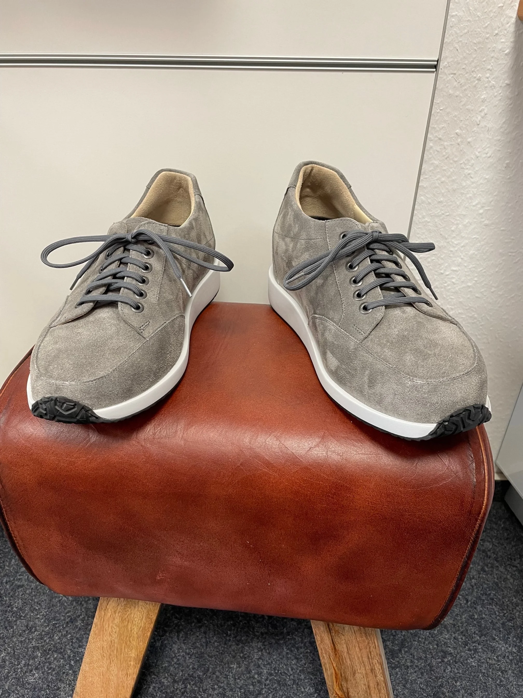 Graue Sneakers mit weißen Sohlen auf einem braunen Hocker