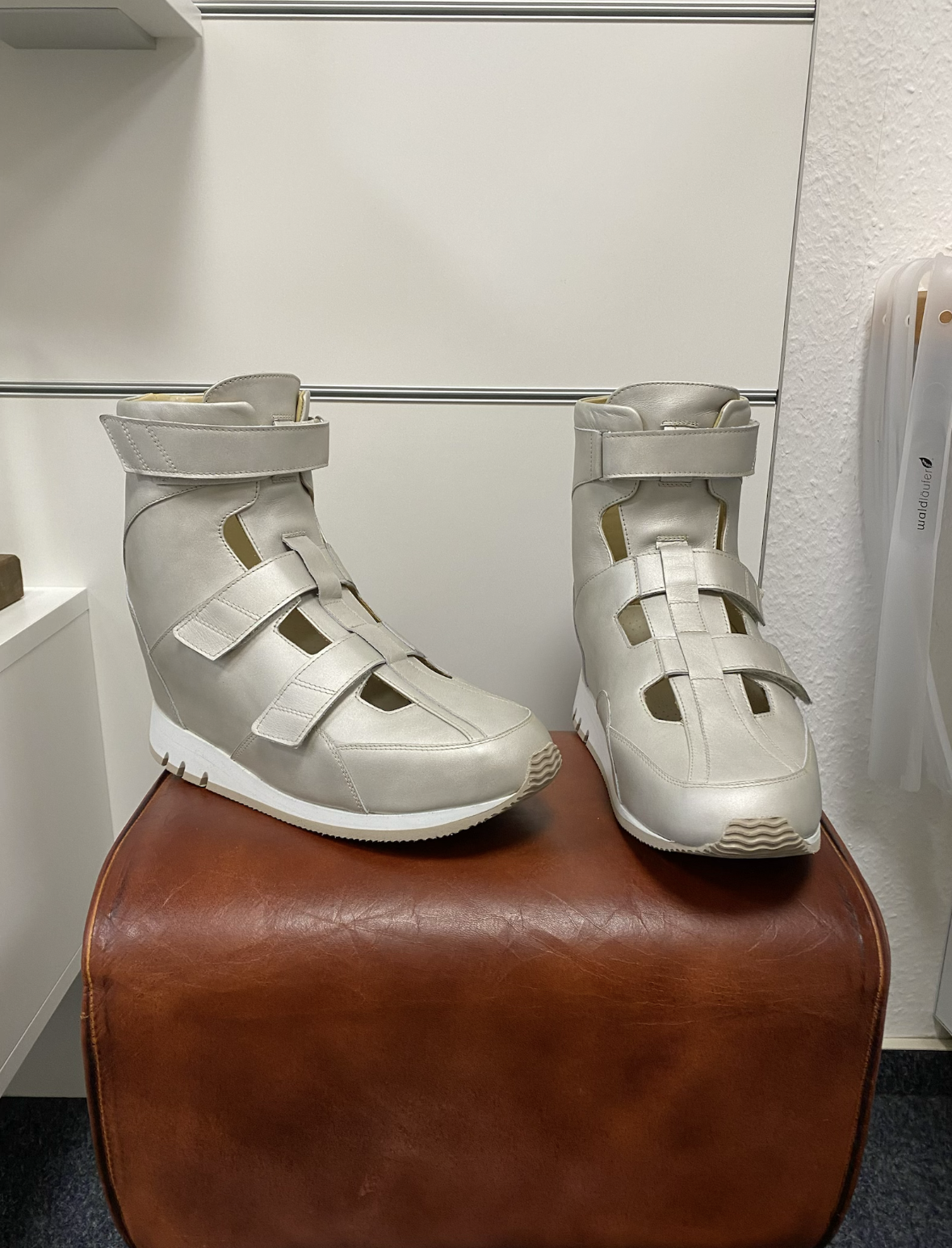 Ein Paar weiße Sneakers mit Klettverschlüssen auf einem braunen Ledersitz.