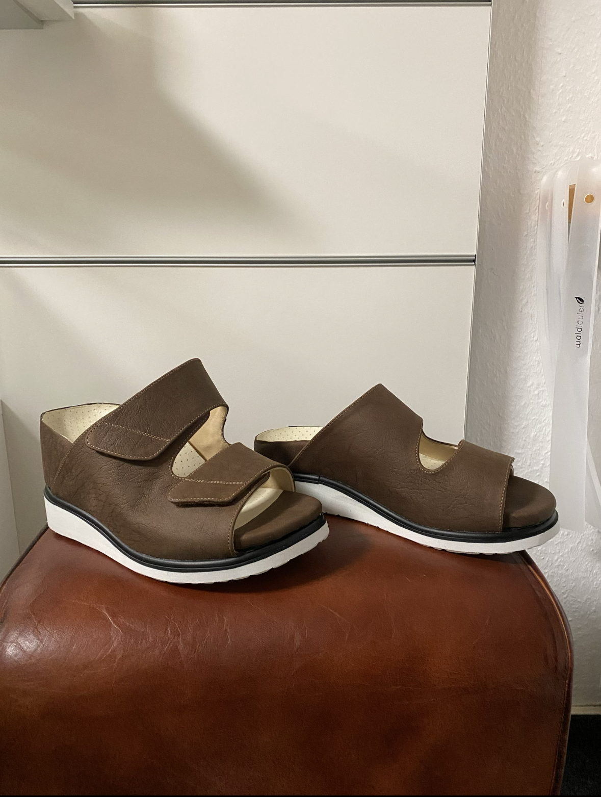 Paare braune Ledersandalen mit Klettverschlüssen auf einem roten Hocker.