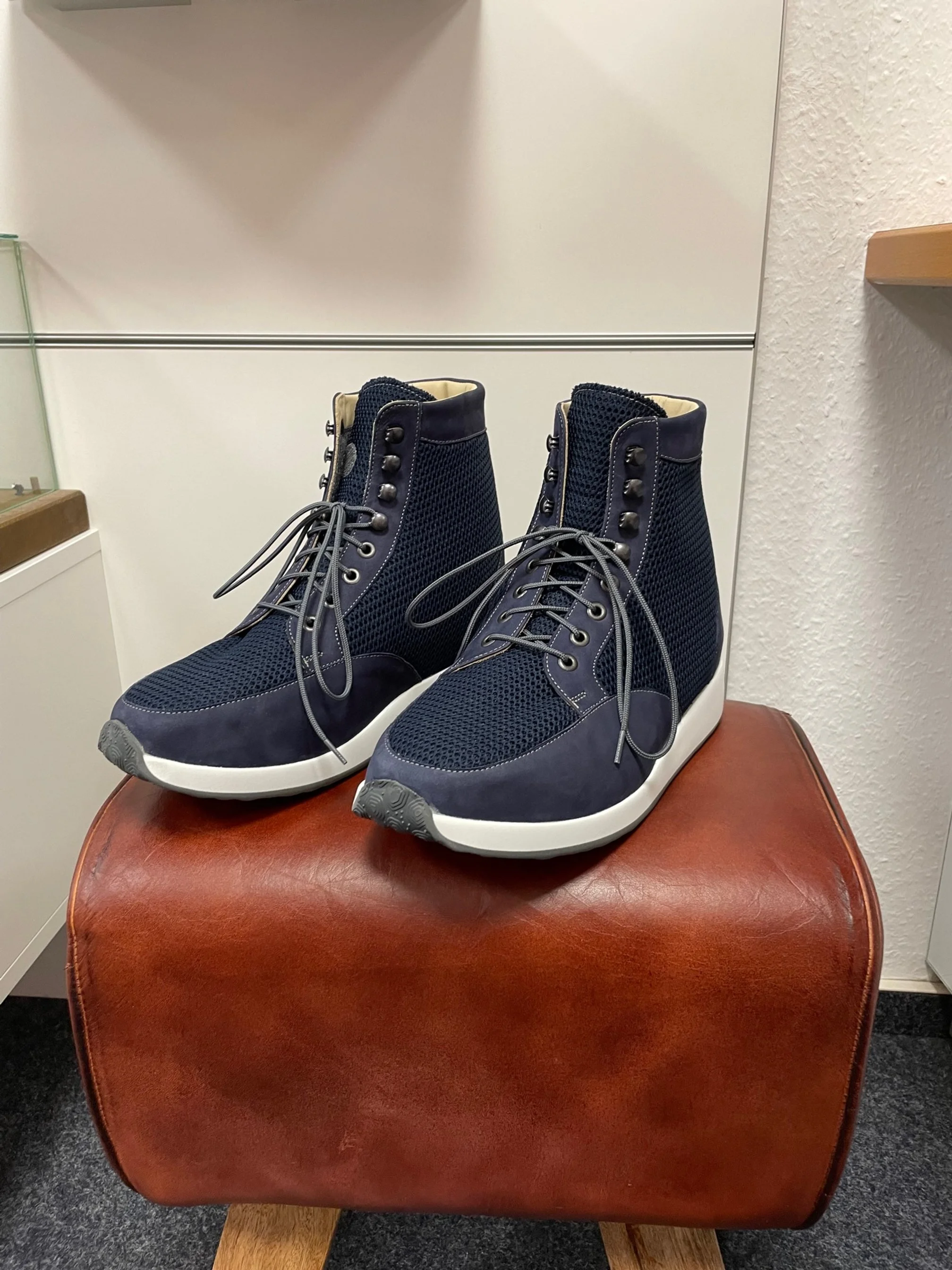 Ein Paar dunkle Sportschuhe auf einem braunen Hocker, im Hintergrund weiße Wände.