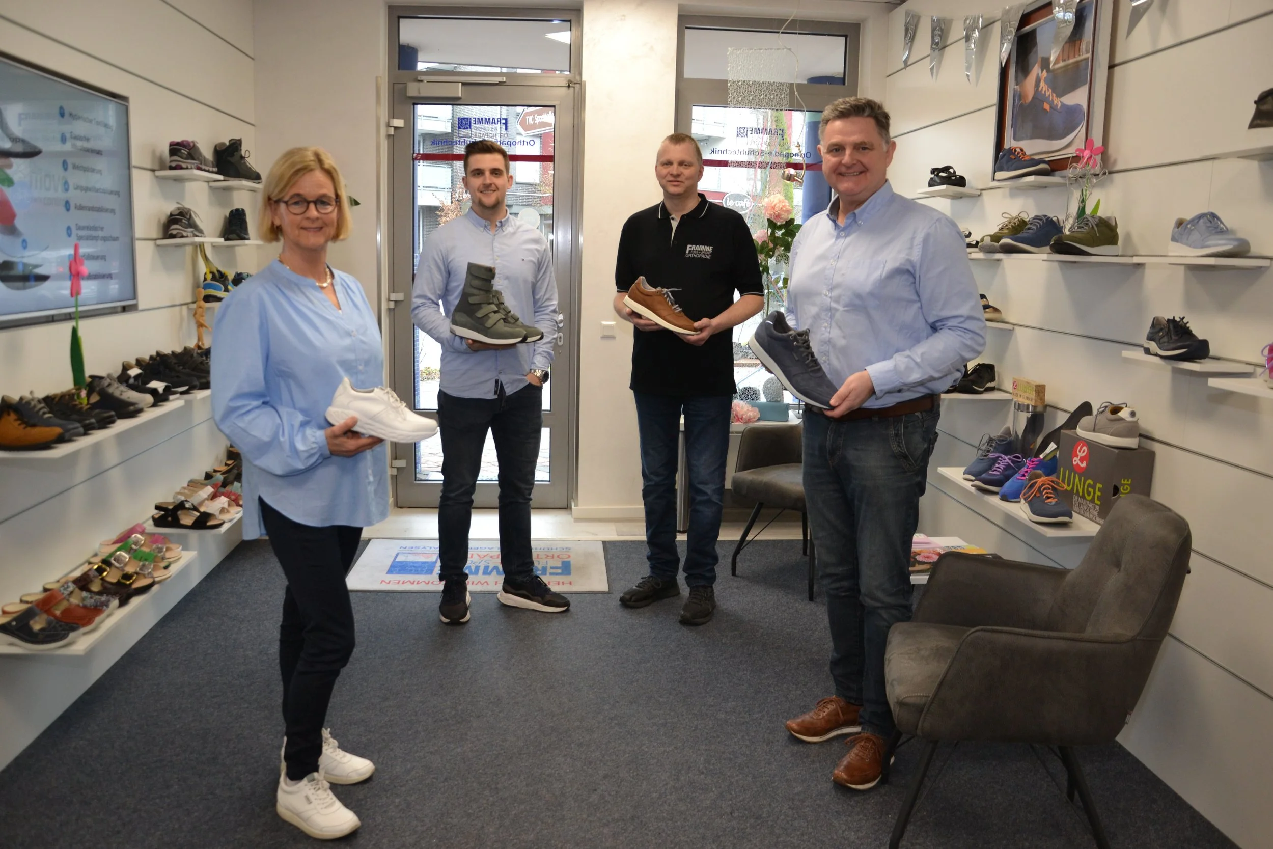 Vier Personen stehen in einem Schuhgeschäft, Links Birgit Framme rechts daneben Linus Framme Orthopädieschuhmachermeister. Ganz rechts steht Inhaber und Orthopädieschuhmachermeister Josef Framme und links daneben sein Geselle Josef Preut