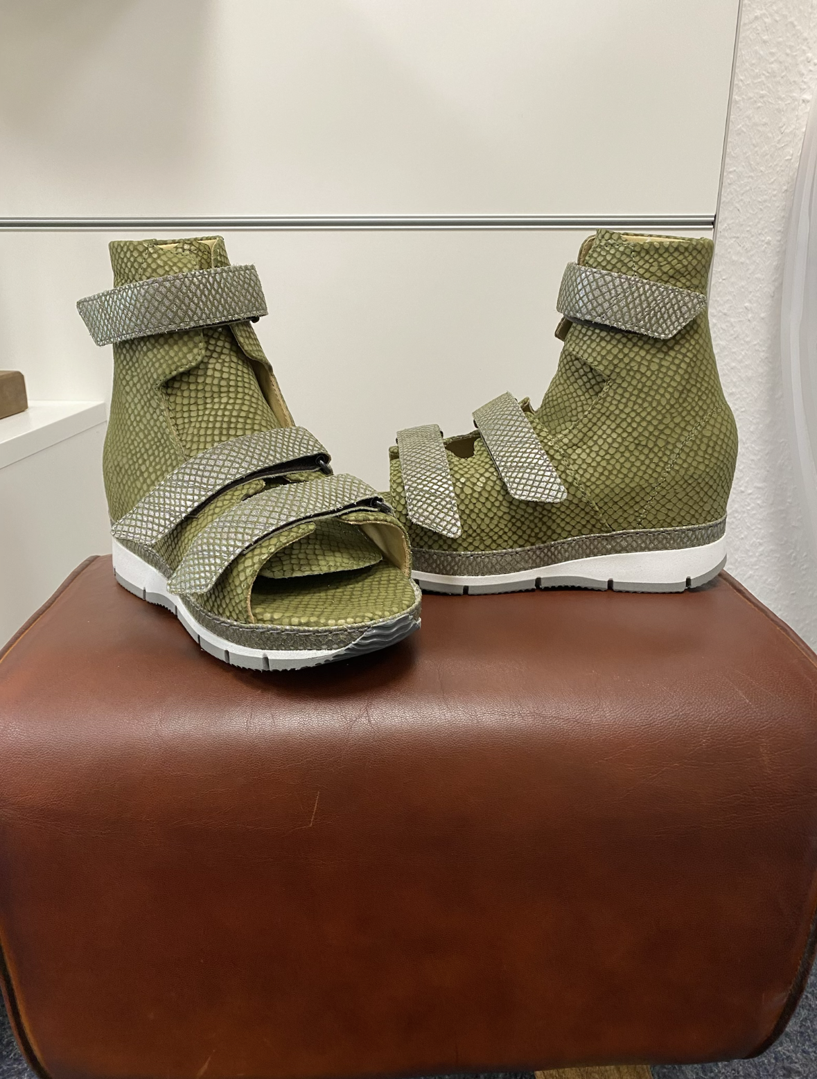 Grüne Sandalen mit mehreren Klettverschlüssen, auf einem braunen Sitzmöbel