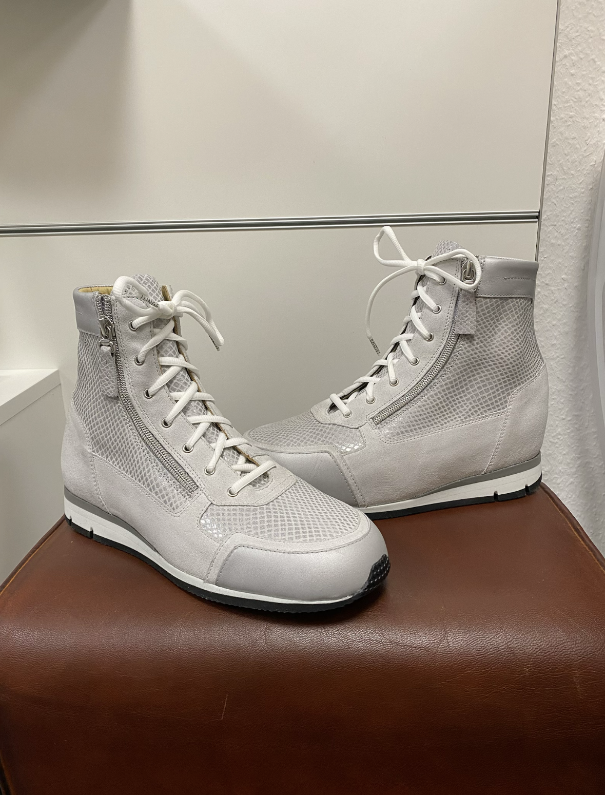 Weiße High-Top-Sneaker aus Mesh- und Lederüberzug mit Reißverschluss an der Seite, auf braunem Lederhocker