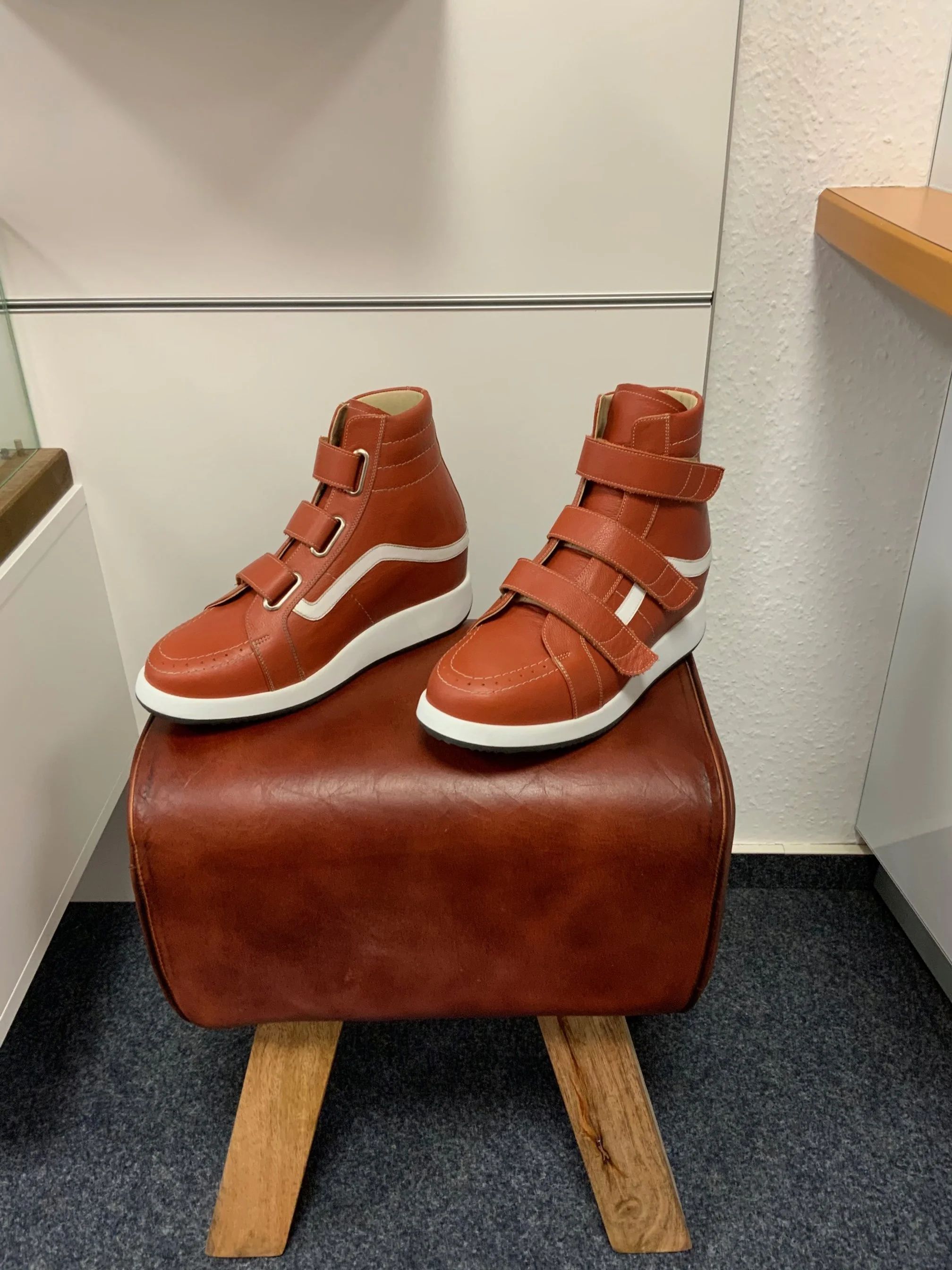 Rote Sneakers mit weißen Streifen und Klettverschlüssen auf einem braunen Hocker.