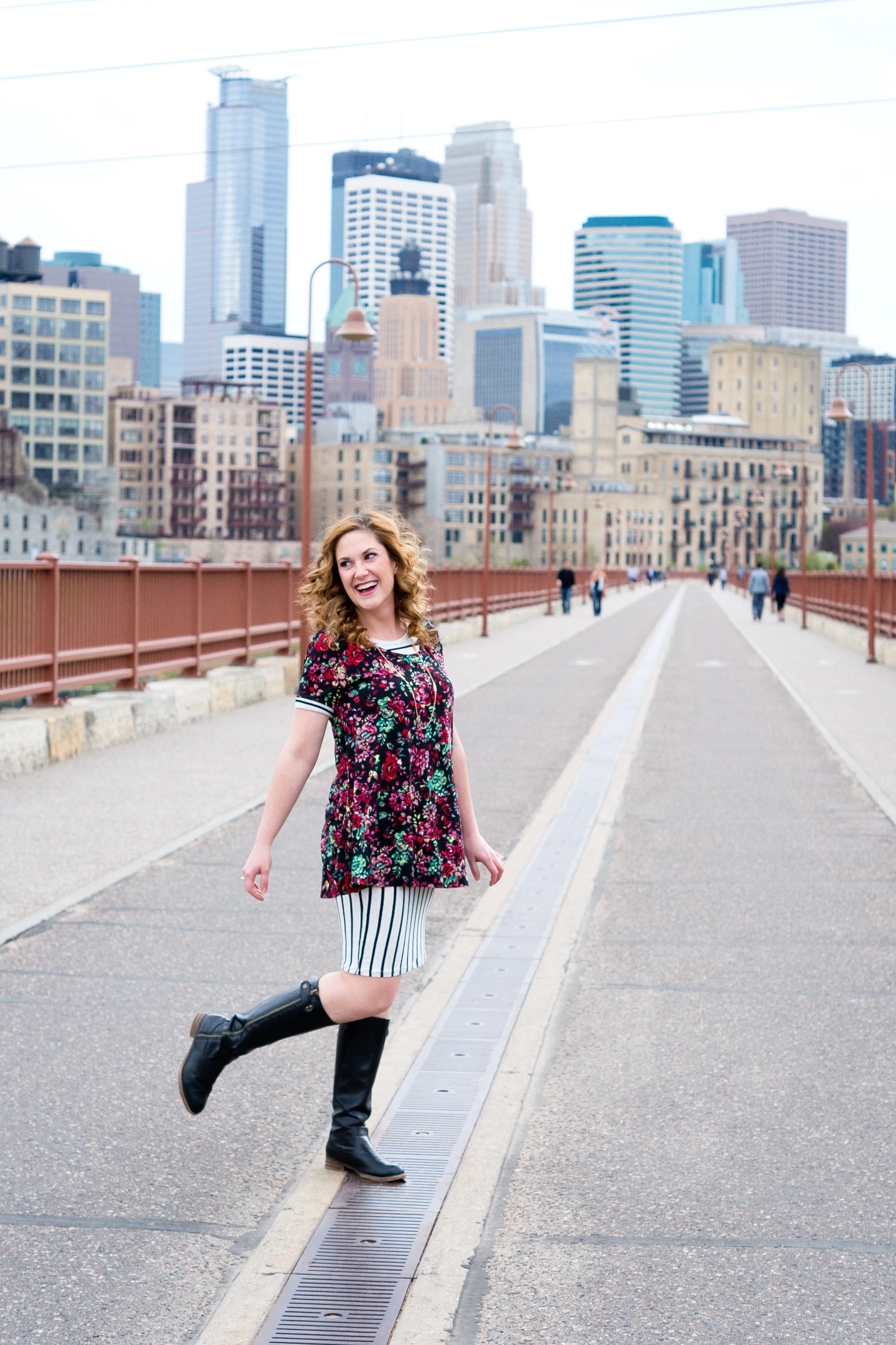 Woman standing on a bridge with city skyline in the background, representing encouragement and hope for grieving mothers after child loss