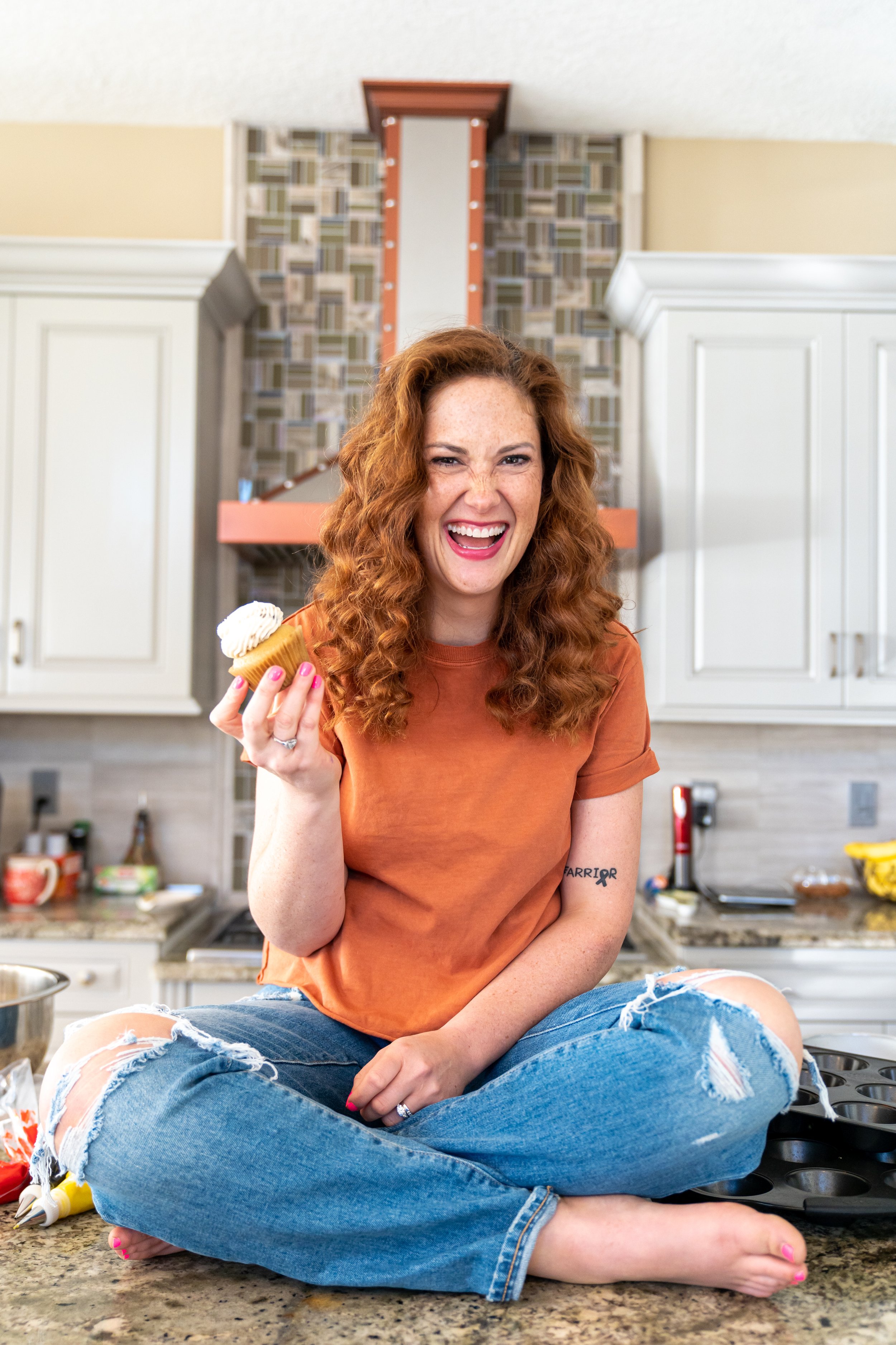 Woman laughing in a modern kitchen while holding a cupcake, representing hope and encouragement for grieving mothers after child loss