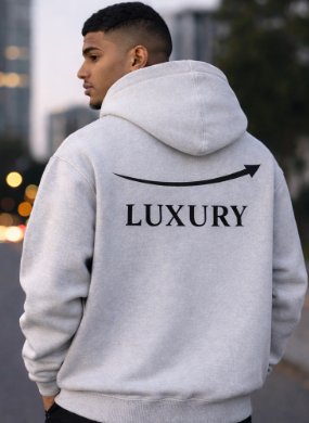 A young man wearing a gray hoodie with the word 'LUXURY' and an arrow design on the back, standing outdoors in an urban environment.