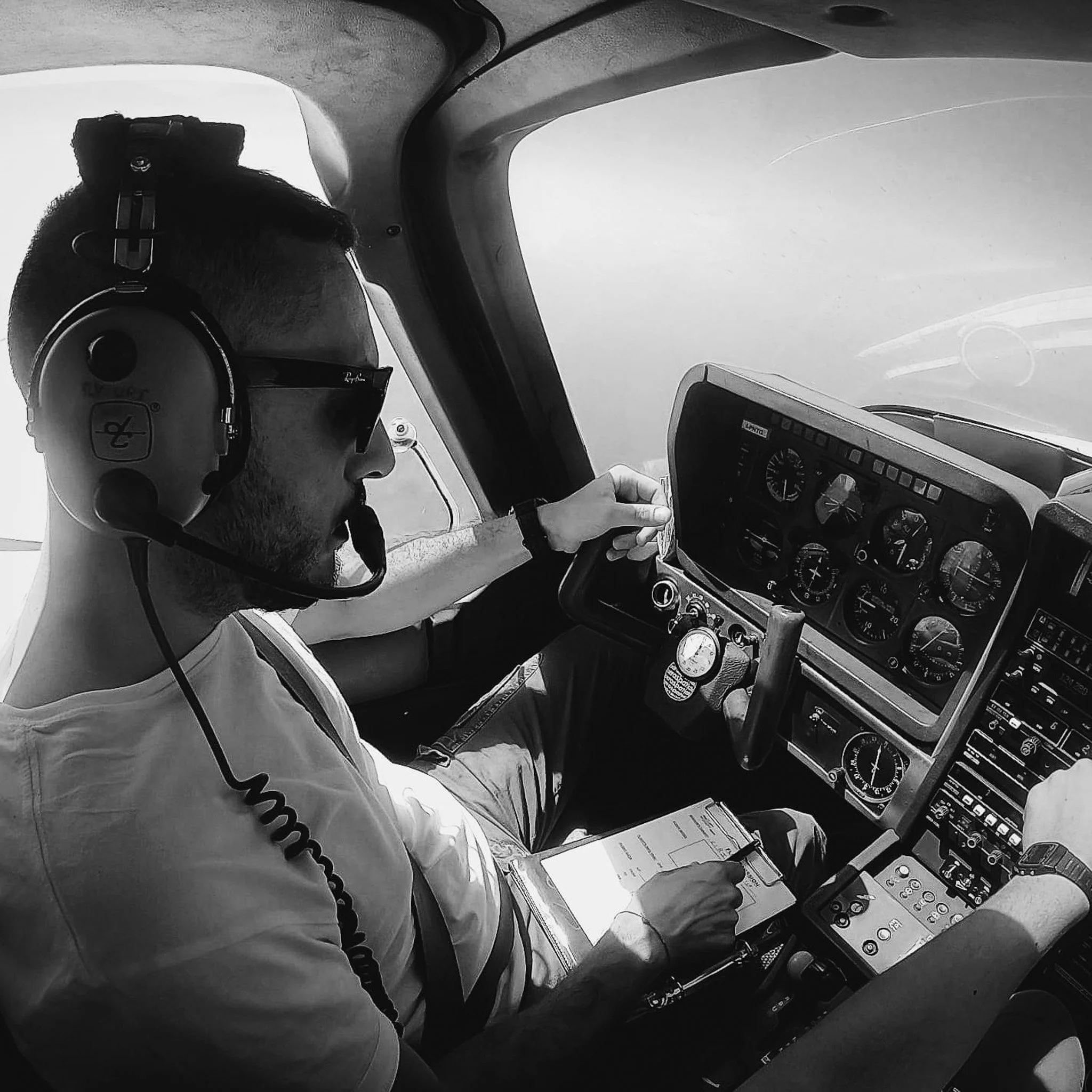 Pilota di aereo al comando, indossa cuffie e occhiali da sole, seduto dietro il pannello di controllo dell'aeromobile.