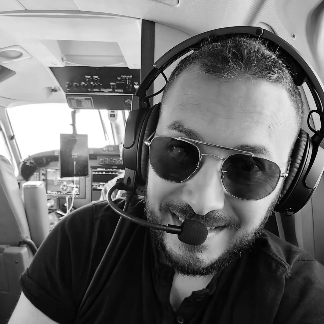 Uomo sorridente con occhiali da sole e cuffie da pilotaggio seduto all'interno di un aereo.