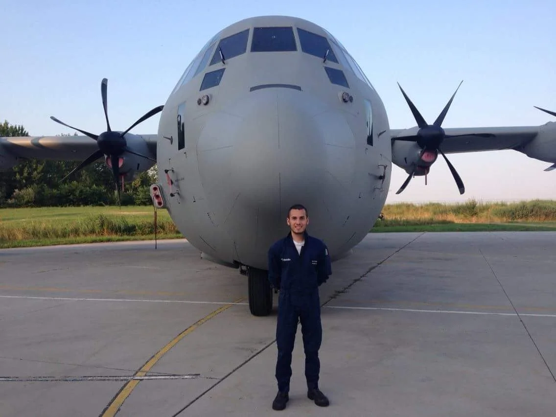 Un uomo in uniforme militare si trova davanti a un grande aereo di alimentazione militare in un aeroporto.