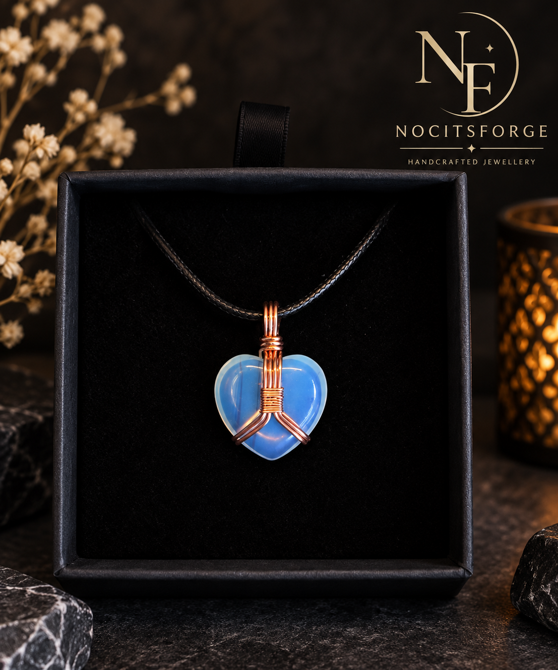 Blue heart-shaped stone pendant wrapped in copper wire, hanging from a black cord and displayed in a black jewellery box by Noctis Forge Jewellery.