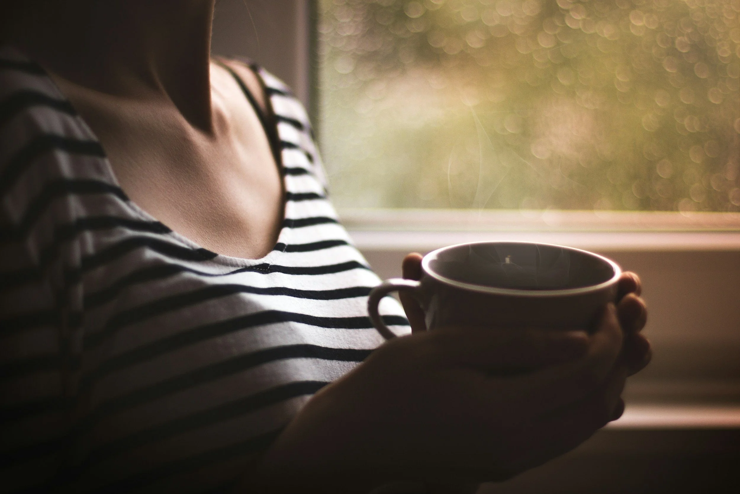 Woman sitting quietly by a window with morning light and coffee, looking peaceful during a life transition