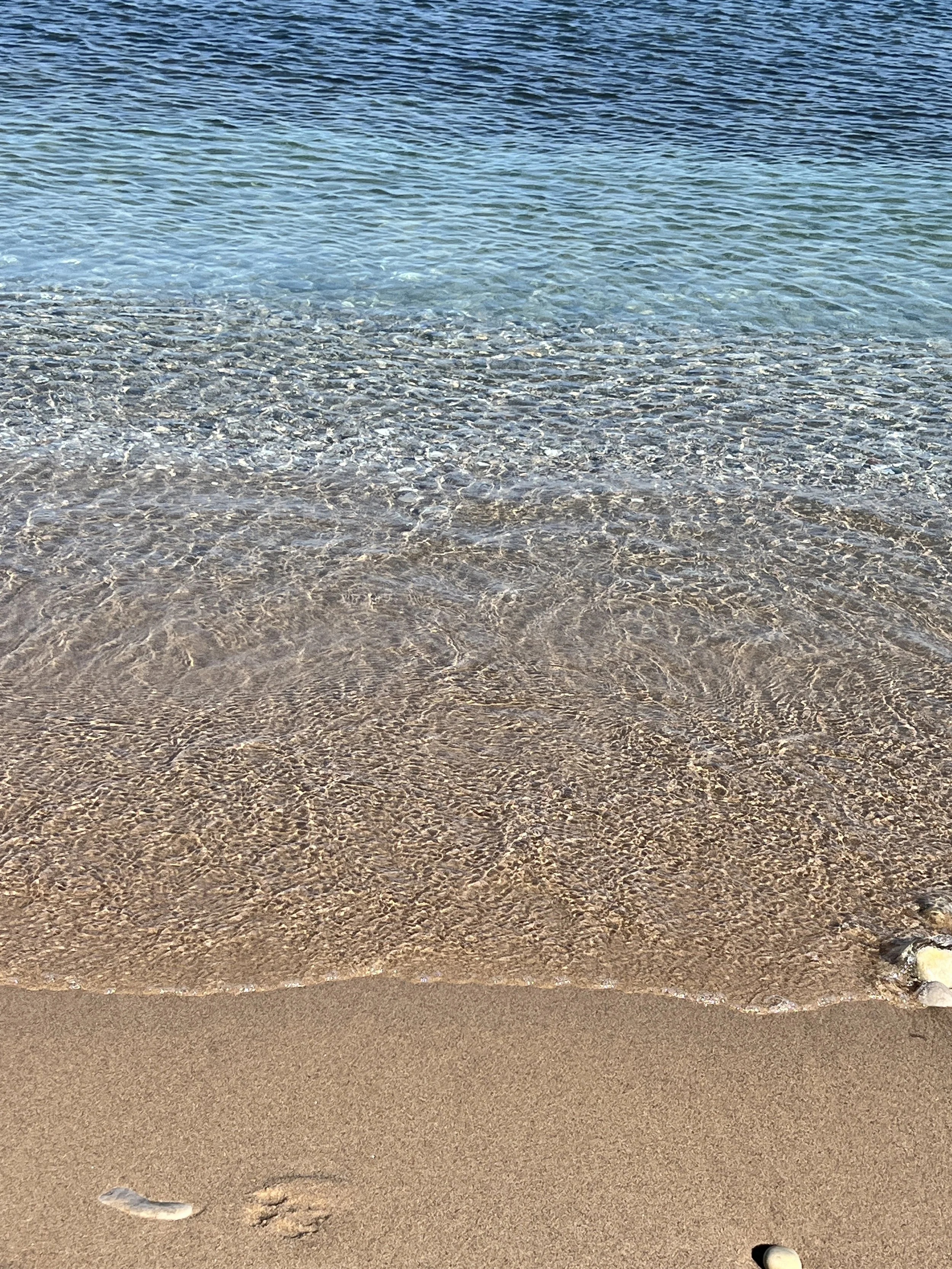 A sandy beach with gentle waves lapping onto the shore and clear blue water in the background.