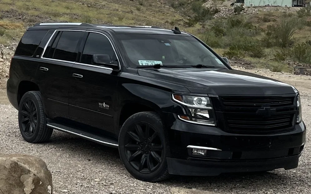 Black SUV parked on gravel with a Texas license plate, mountainous terrain in the background.