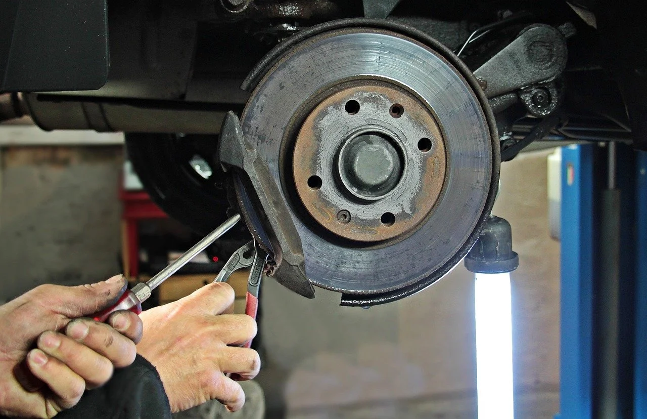 Hands using a screwdriver and pliers to work on a car's brake disc assembly in a workshop.