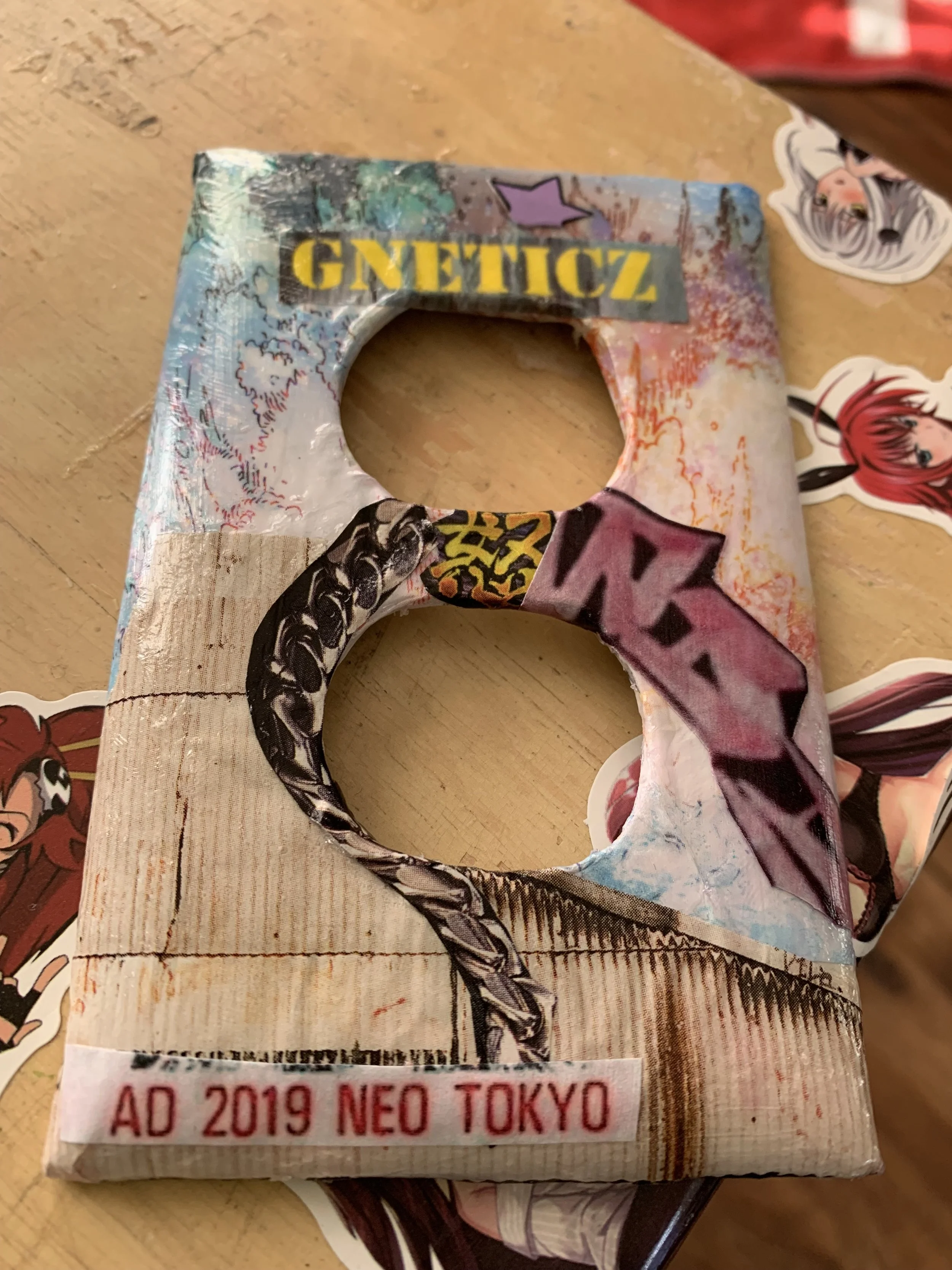 Decorative cardboard number 8 with graffiti-style text, artwork, and stickers, placed on a wooden surface surrounded by anime character stickers.