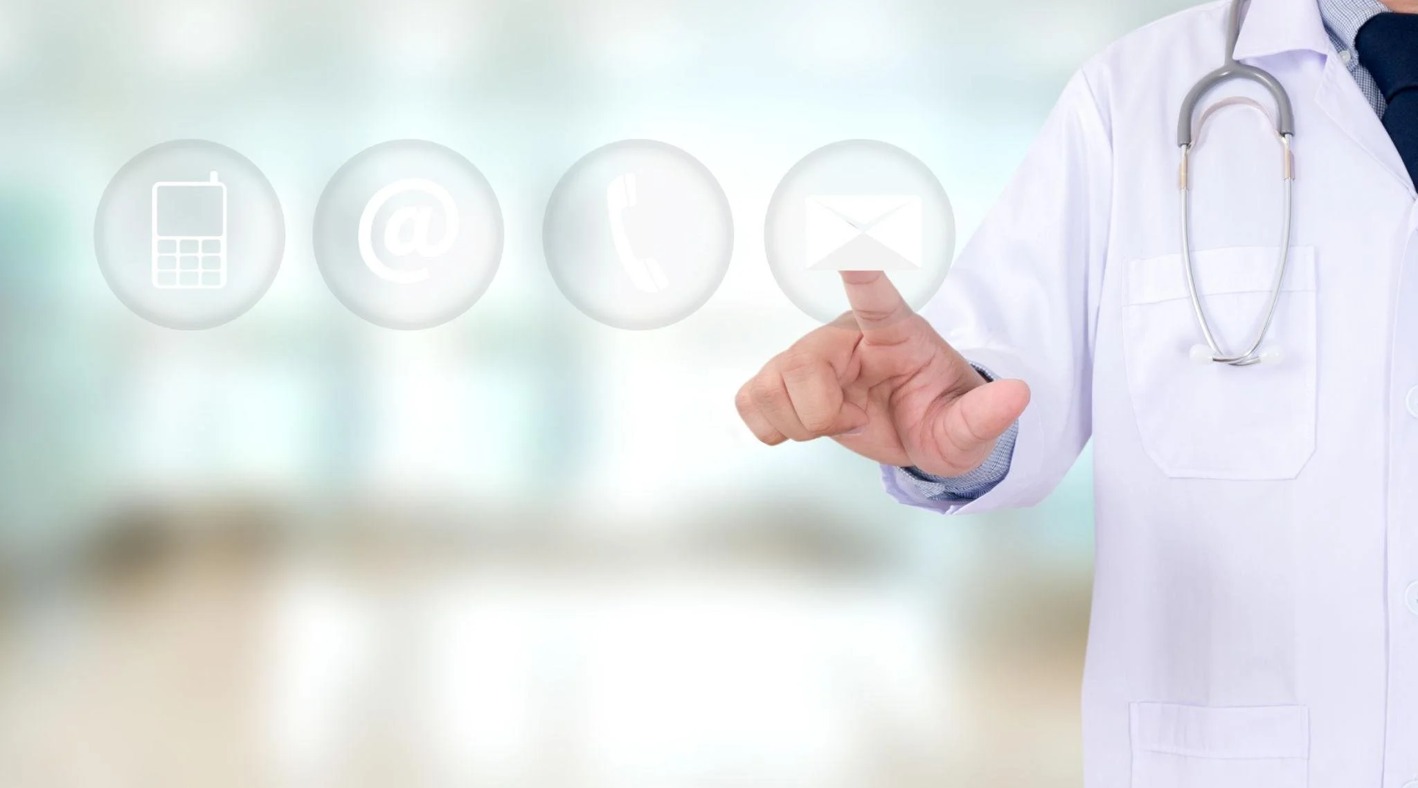 A doctor in a white coat with a stethoscope around their neck points at a virtual touchscreen interface displaying icons for phone, email, and messaging.