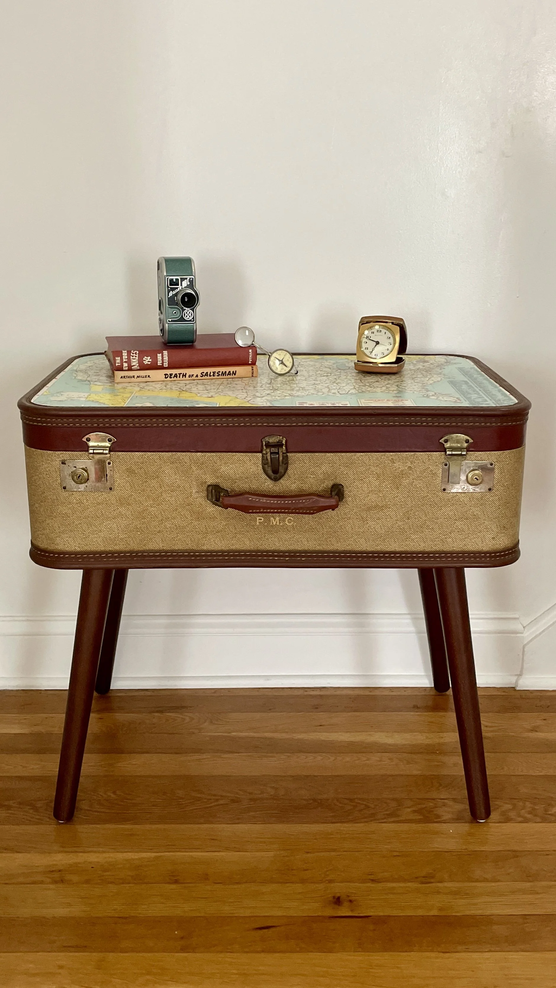 Vintage suitcase table with travel-themed objects on top, including books, a camera, clocks, and a map design on the surface.