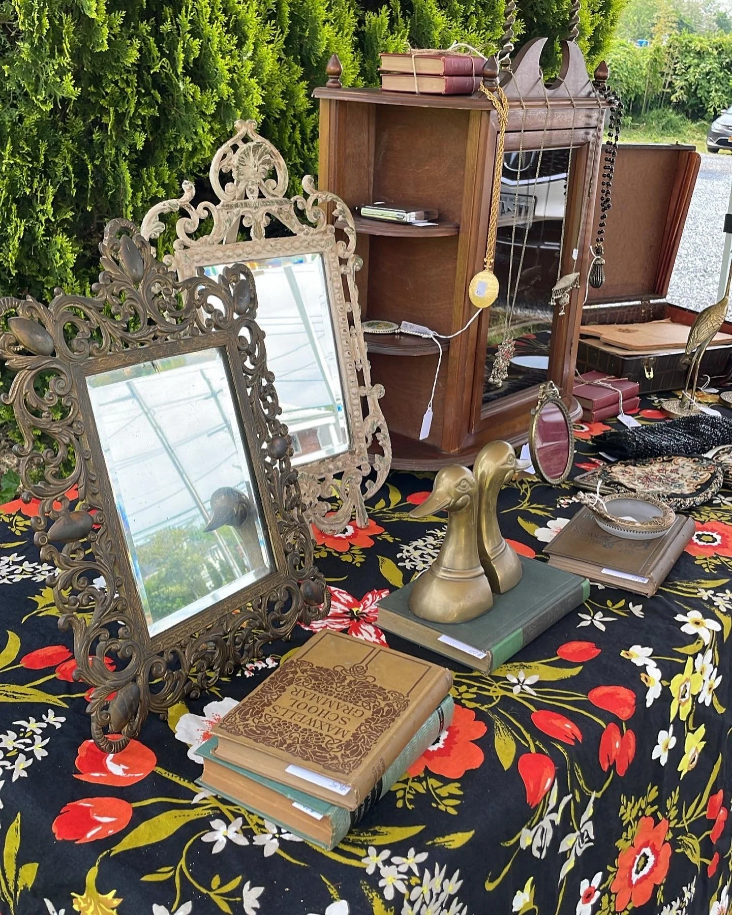 Tables with vintage mirrors, books, jewelry, and decorative items at an indoor or outdoor flea market or antique sale.