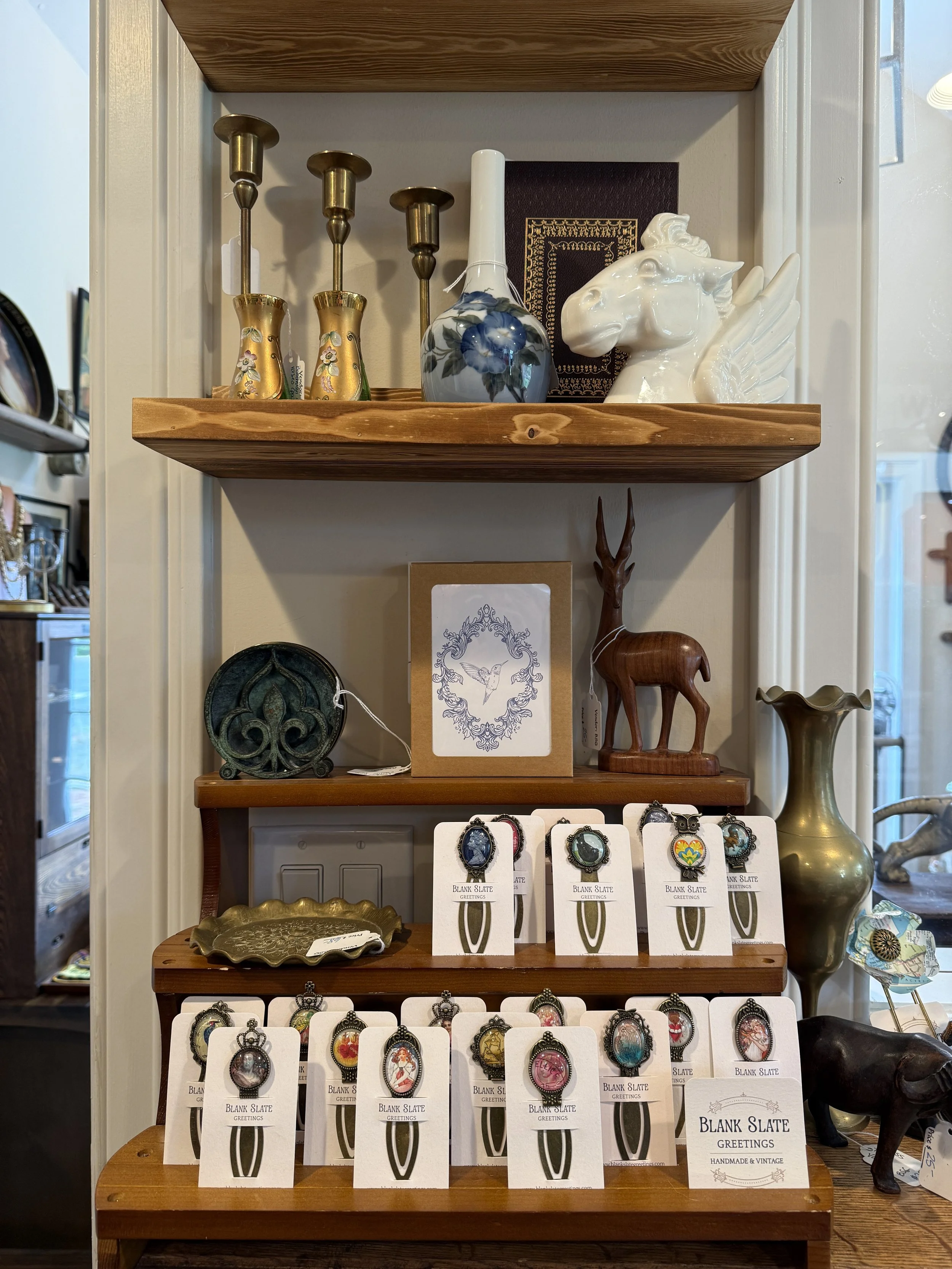 Display of various decorative items and jewelry, including rings and pendants, on wooden shelves.