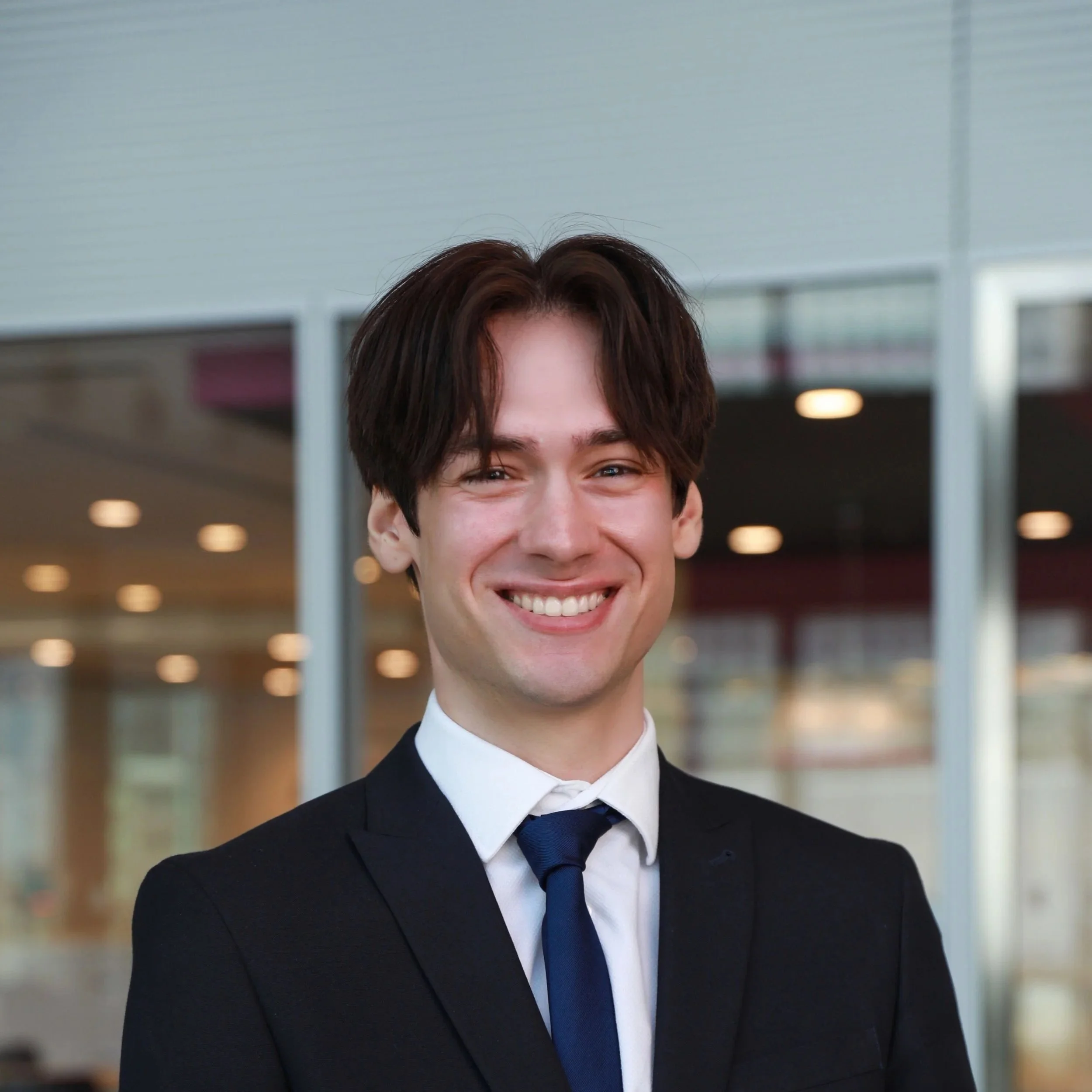 Smiling young man in a business suit and tie in front of an office building.