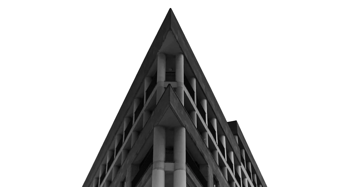 Black and white photograph of a modern multi-story building with a triangular shape, featuring rectangular windows and concrete columns.