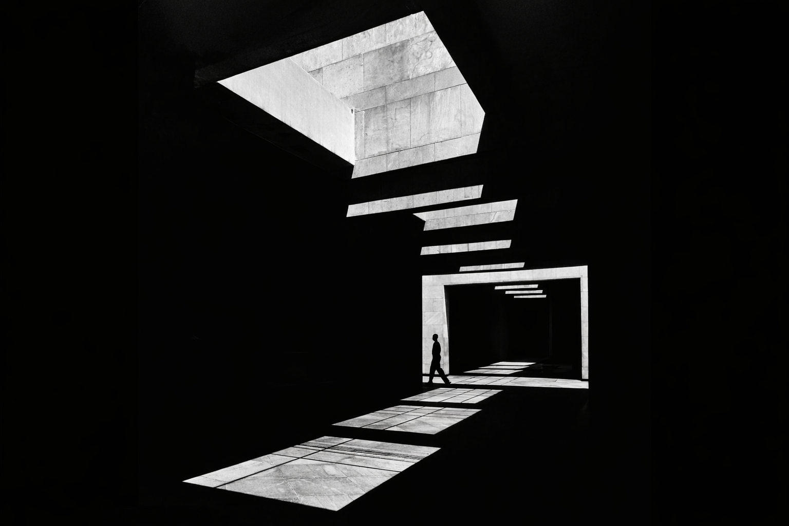 A person walking through a modern, minimalist space with stark black walls and large geometric openings allowing natural light to cast patterned shadows on the floor.