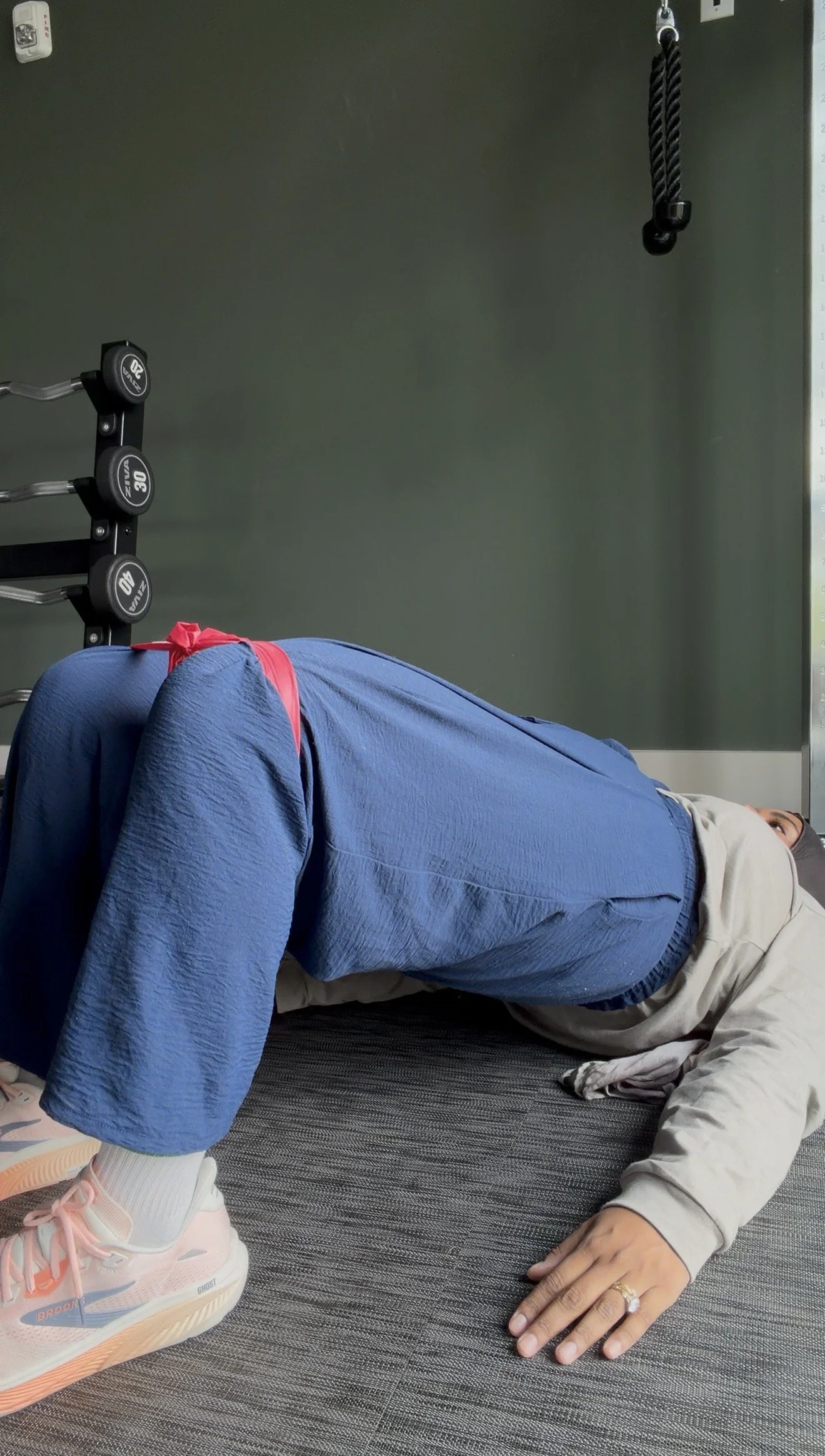 Person lying on the floor in workout attire, near gym equipment, with a dark wall background.