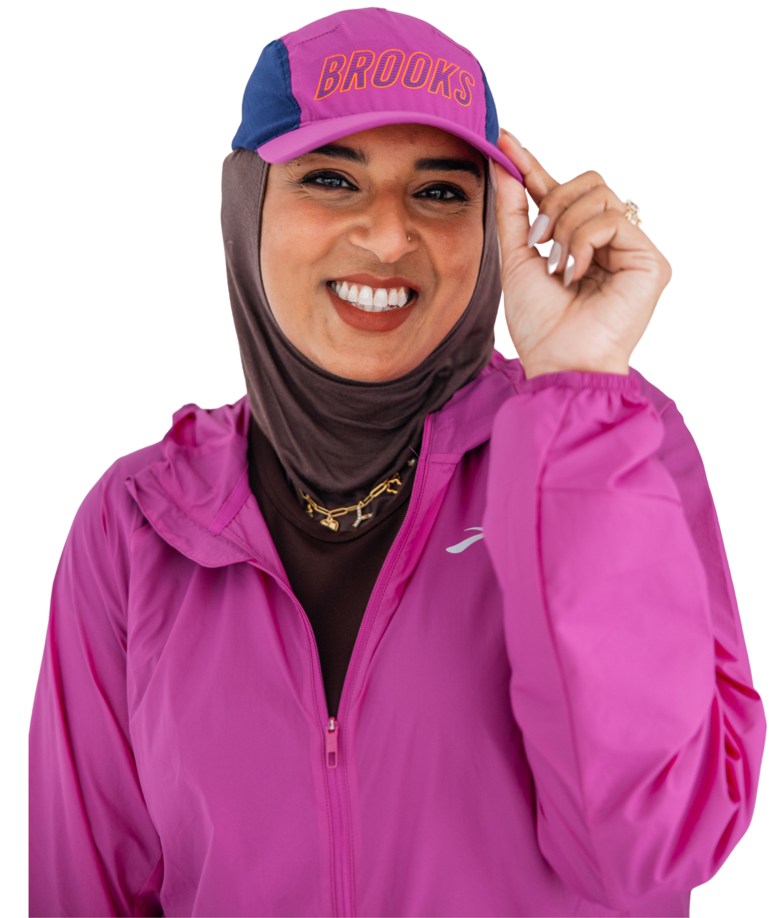 A woman wearing a purple and pink Brooks cap and matching pink jacket smiling and holding the cap with her right hand.