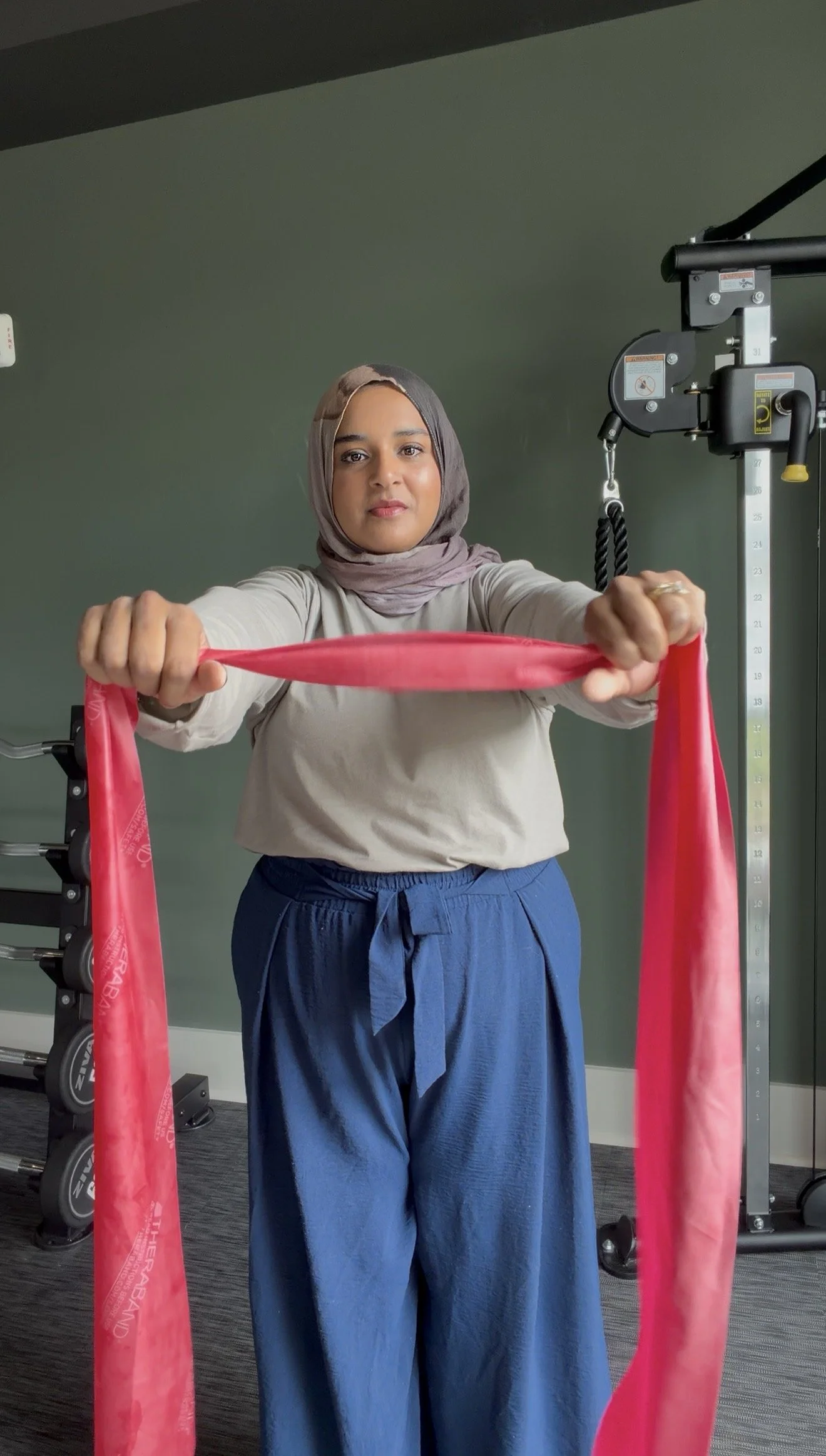 A woman in a hijab and casual clothing using resistance bands during a workout in a gym.