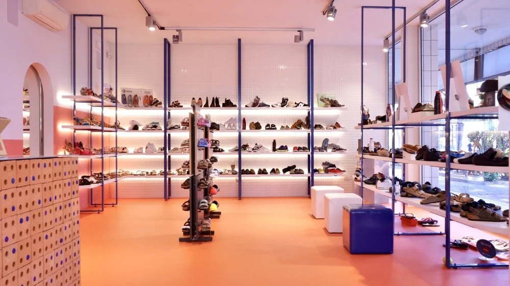 Interno di un negozio di scarpe con scaffali pieni di calzature esposte e sedie per i clienti.