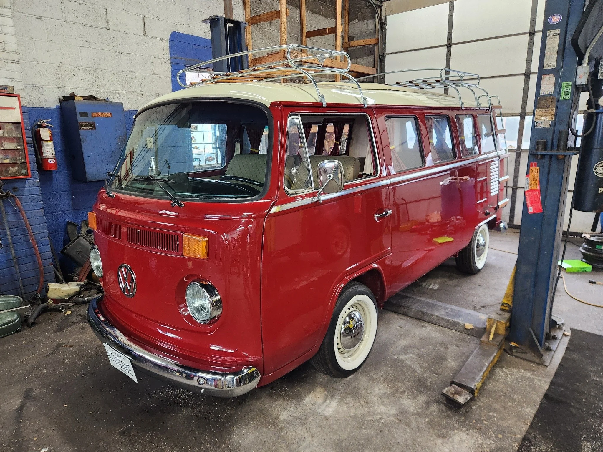 Red vintage Volkswagen Type 2 van with a white roof and roof racks, parked inside a garage.