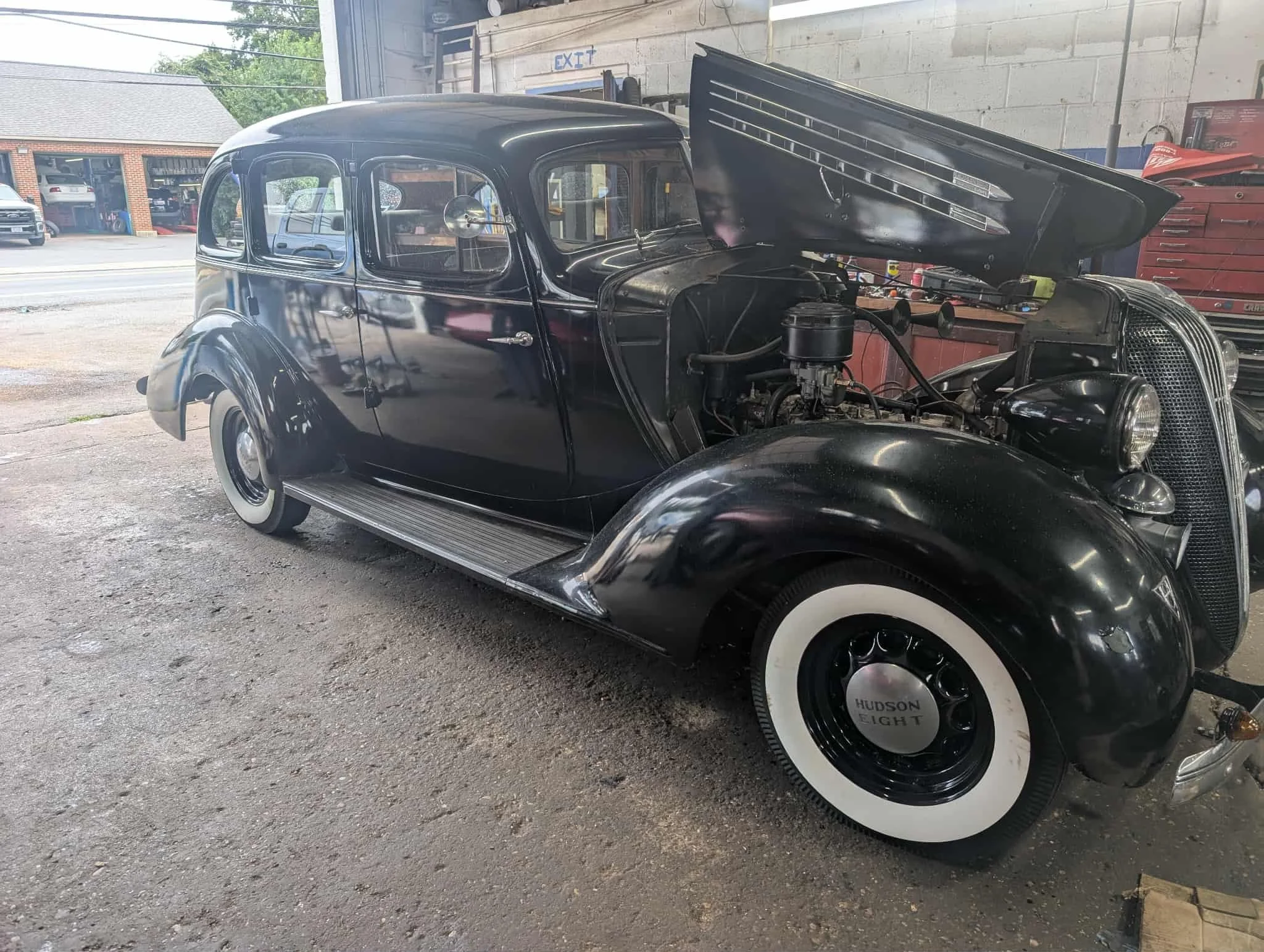 A vintage black car with its hood open inside a garage or workshop.