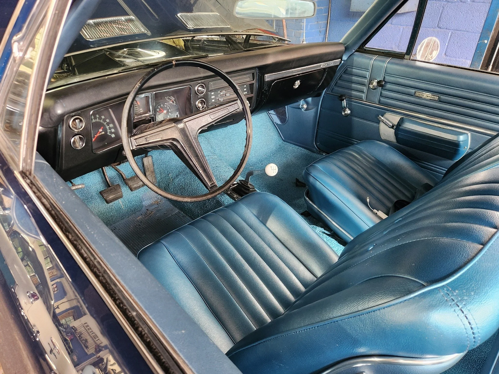 Interior view of a vintage car with blue seats, dashboard, and steering wheel, featuring an analog instrument panel and a manual gear shift.