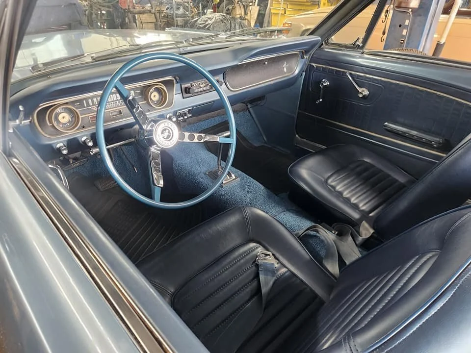 Interior of a vintage car with black seats, a light blue steering wheel, and a dashboard with analog gauges.